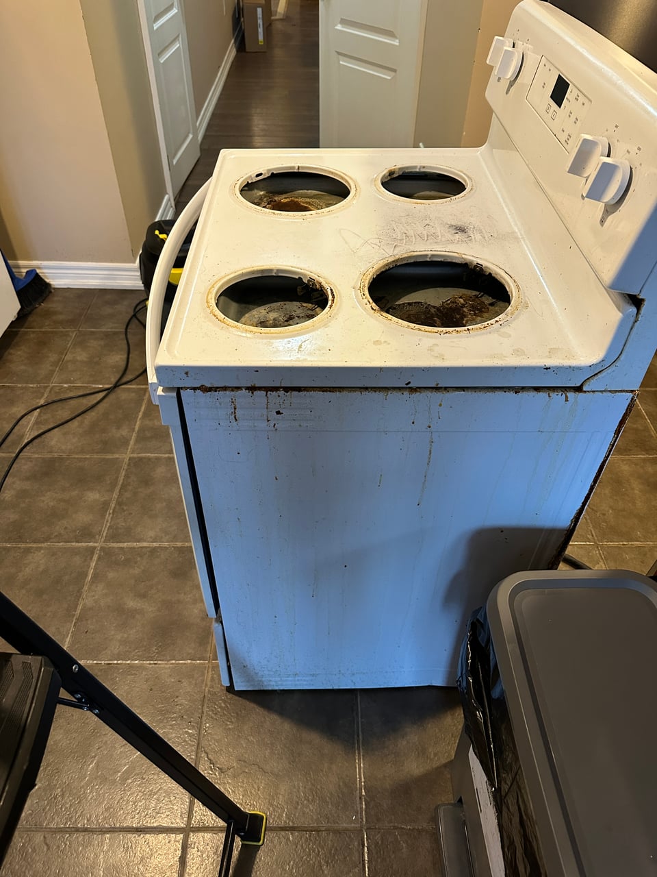 White electric stove with brown buildup around the burner openings and streaks down the side panel.